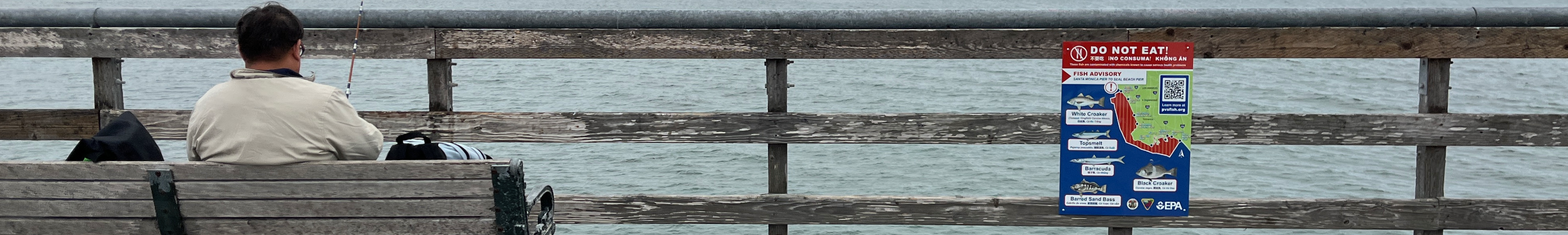 Person fishing on the pier with a cautionary sign beside him